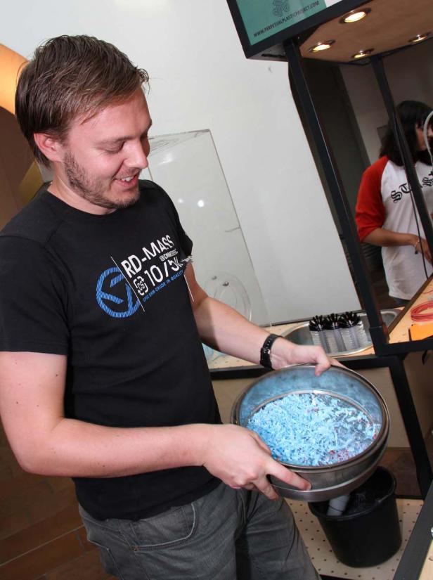 Ein Mann hält einen Sieb mit blauen Kunststoffspänen in den Händen.