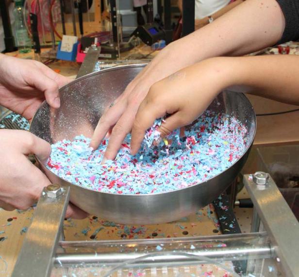 Mehrere Hände mischen blaue und rote Konfetti in einer Metallschüssel.