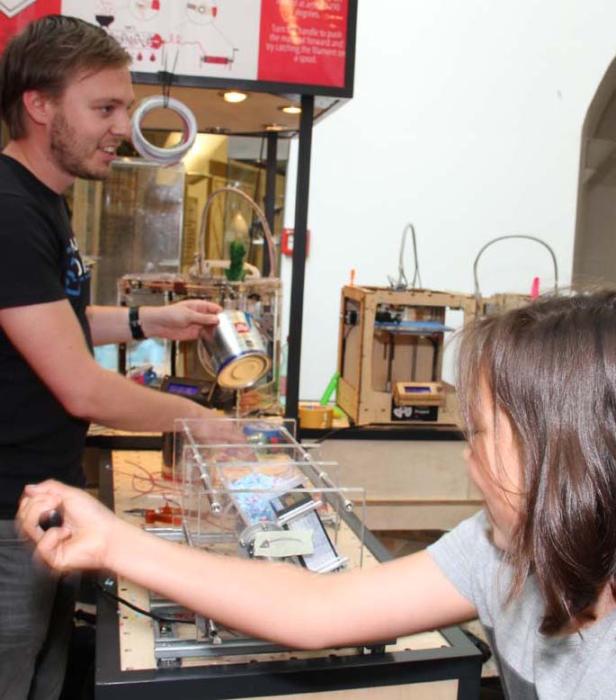 Ein Mann gießt etwas aus einer Dose in eine Maschine, während ein Kind zusieht.