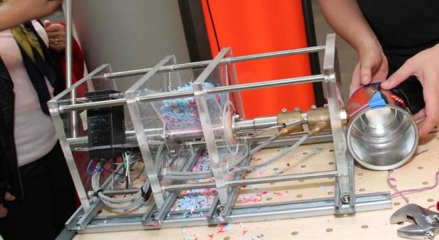 Eine Maschine verarbeitet blaue und rosa Plastikflocken zu einem neuen Produkt.