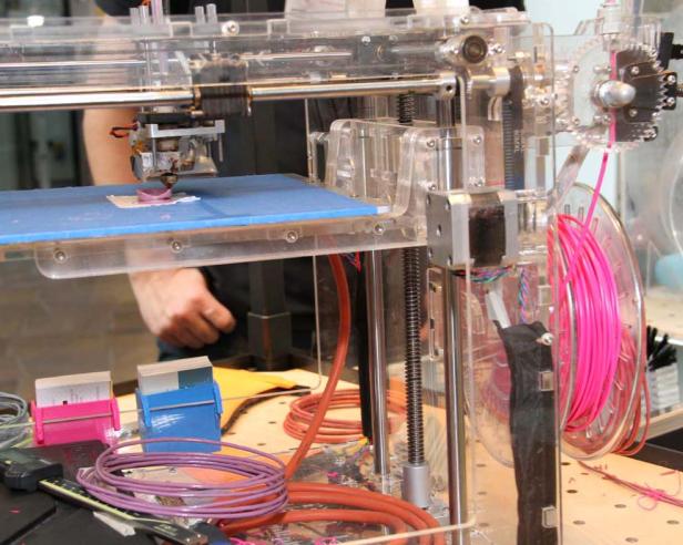 Ein 3D-Drucker druckt ein kleines, rosafarbenes Objekt.