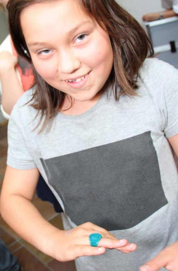 Ein junges Mädchen mit braunen Haaren und einem türkisfarbenen Ring lächelt.