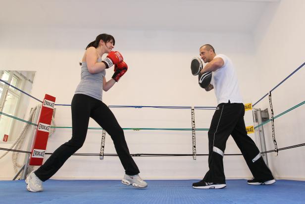 Eine Frau boxt mit einem Trainer in einem Boxring.