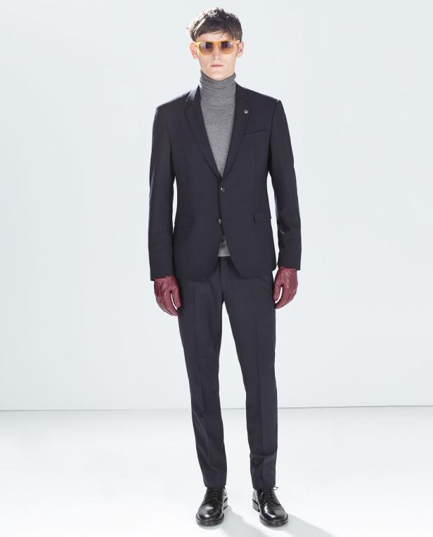 Ein Mann mit Sonnenbrille, Anzug und roten Handschuhen steht vor einem weißen Hintergrund.