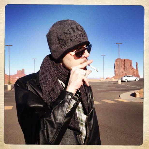 Ein Mann mit Mütze und Sonnenbrille raucht vor dem Monument Valley.