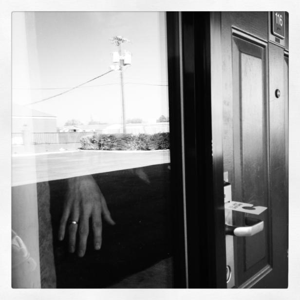 Eine Hand mit Ring spiegelt sich in der Fensterscheibe einer Zimmertür mit der Nummer 116.