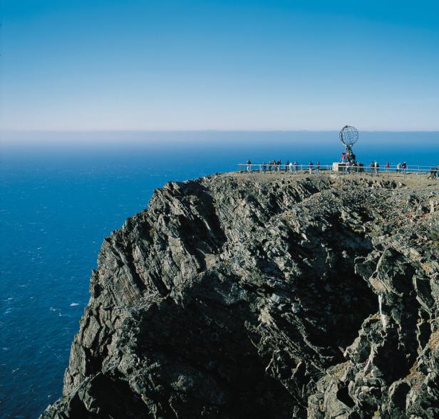 Besucher stehen am Nordkap-Plateau mit dem Globus-Denkmal am Rande einer Klippe.