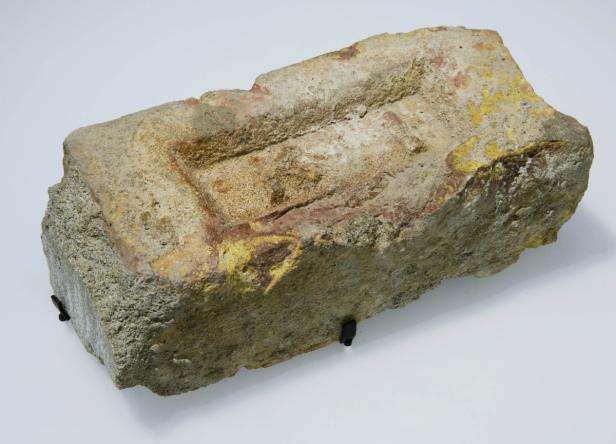 Ein alter, abgenutzter Ziegelstein mit gelben und roten Verfärbungen.