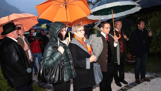 Eine Gruppe von Menschen steht im Regen unter Schirmen.