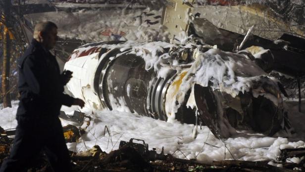 Das Flugzeugwrack ist mit Löschschaum überzogen. Ein Mann geht an den mit Löschschaum bedeckten Trümmern eines Flugzeugs vorbei.