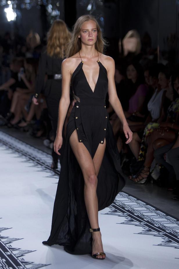 Eine Frau in einem schwarzen Kleid mit hohem Schlitz auf einem Laufsteg.