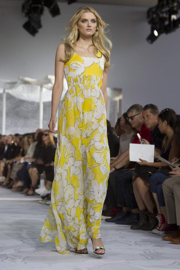 Eine blonde Frau präsentiert ein gelb-weißes Blumenkleid auf dem Laufsteg.