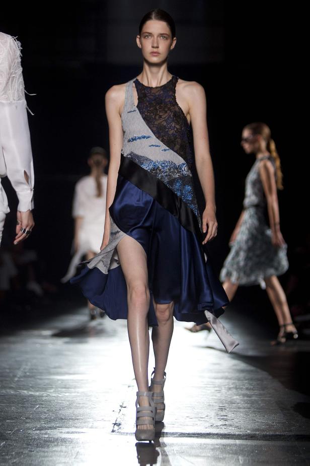 Ein Model präsentiert ein asymmetrisches Kleid mit Spitze und blauem Satin auf dem Laufsteg.