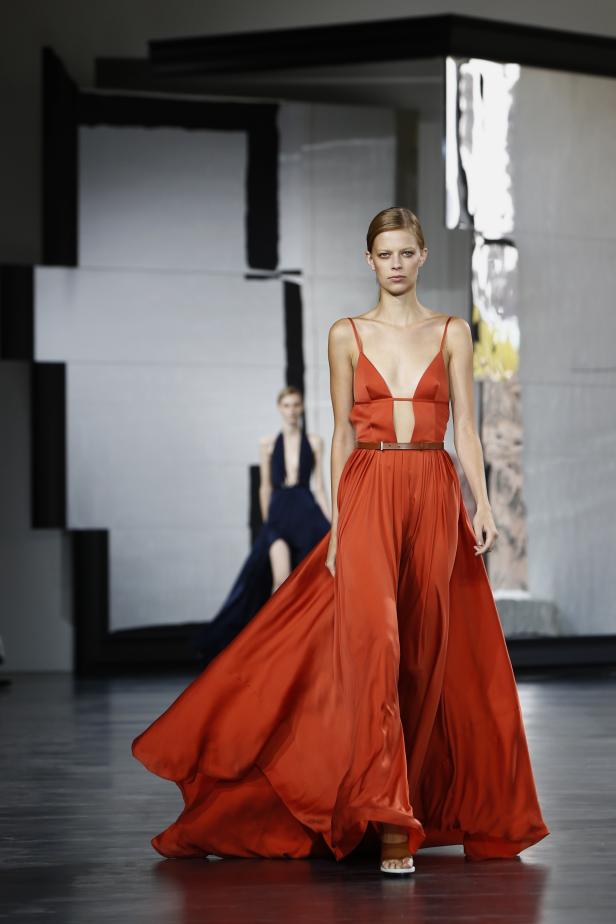 Eine Frau in einem orangefarbenen Hosenkleid auf einem Laufsteg.