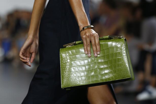 Eine Frau trägt eine grüne Handtasche mit Krokodilmuster und ein goldenes Armband.