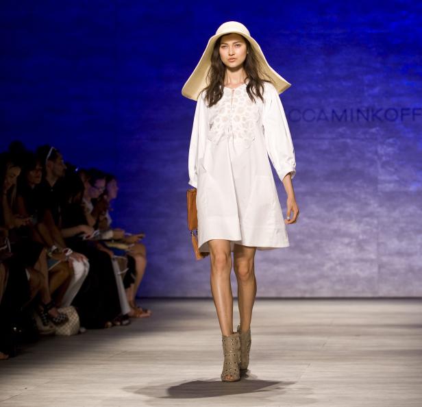 Eine Frau mit Hut und weißem Kleid läuft über einen Laufsteg.