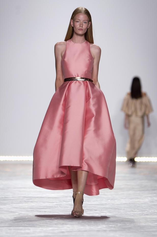 Ein Model präsentiert ein rosafarbenes Kleid mit goldenem Gürtel auf dem Laufsteg.