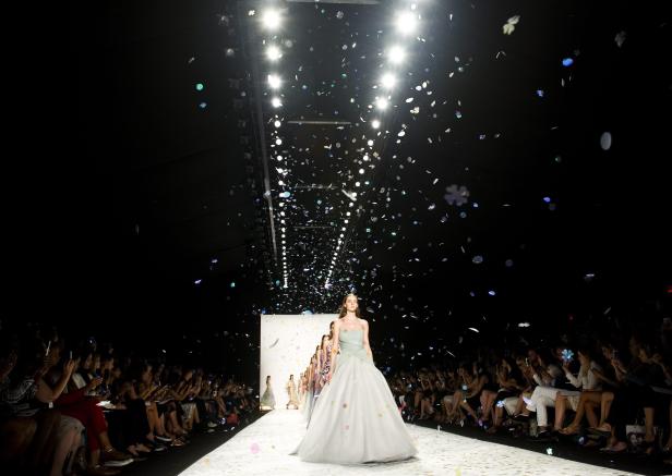 Eine Frau in einem Ballkleid läuft über einen Laufsteg, während Konfetti fällt.
