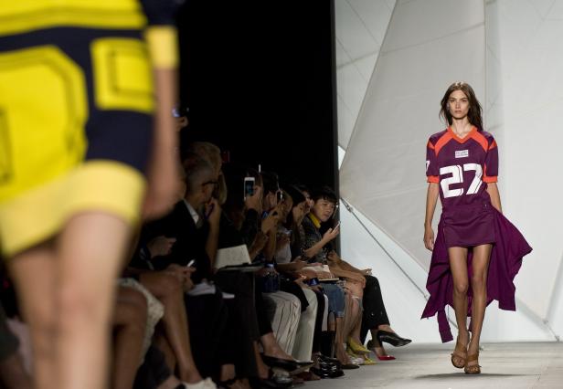 Ein Model präsentiert ein lila-oranges Kleid mit der Nummer 27 auf dem Laufsteg.