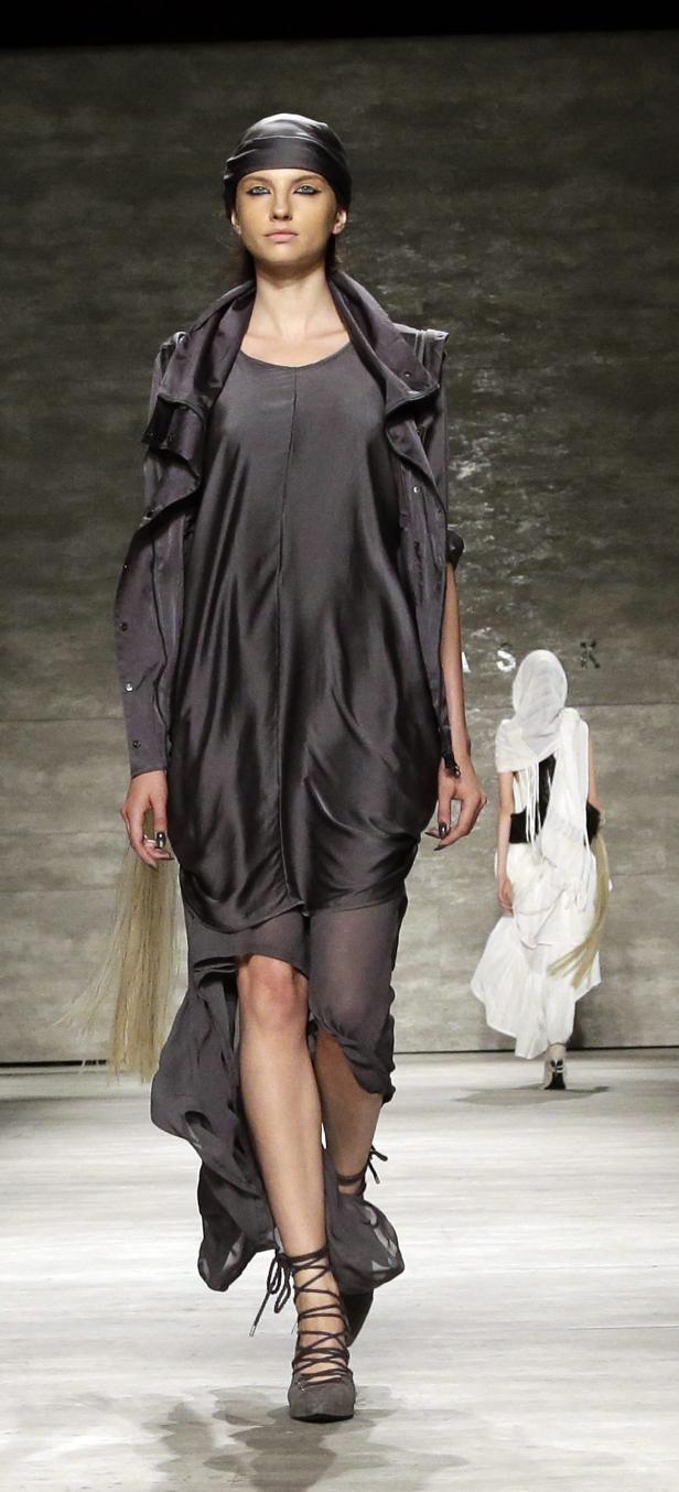 Eine Frau in einem grauen Kleid und Kopftuch läuft auf einem Laufsteg.