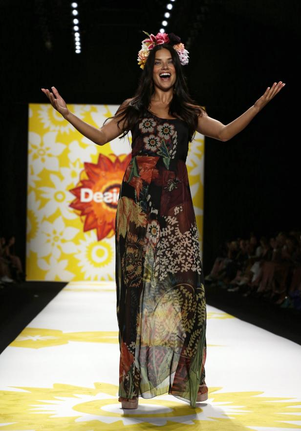 Ein Model mit Blumenkranz präsentiert ein langes, buntes Kleid auf dem Laufsteg.