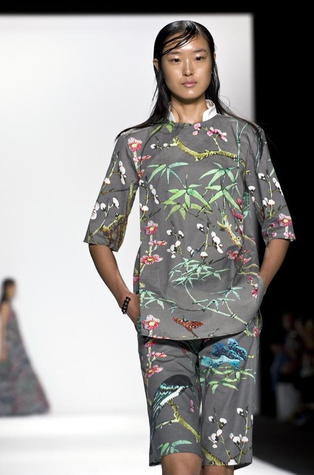 Eine Frau mit nassen Haaren präsentiert ein graues Ensemble mit Blumen- und Vogelmuster.