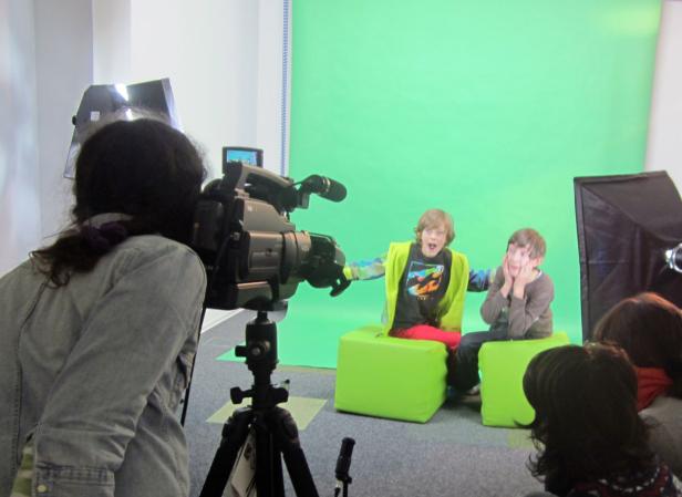 Zwei Jungen sitzen vor einem Greenscreen, während sie gefilmt werden.