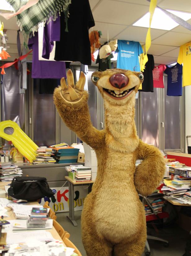 Ein Sid-Kostüm aus „Ice Age“ winkt in einem unordentlichen Büro.