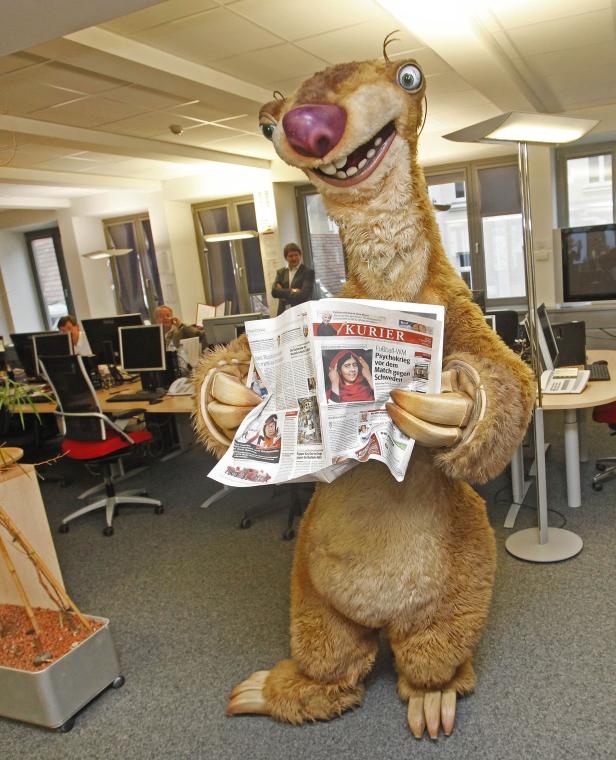 Ein Faultier-Kostüm liest in einem Büro die Zeitung „Kurier“.