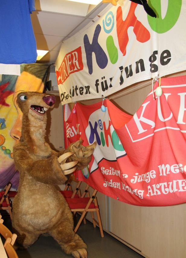 Ein Sid-Kostüm von „Ice Age“ steht vor Bannern mit der Aufschrift „Kiko“.