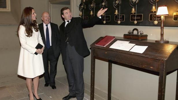 Kate Middleton und zwei Männer vor einer alten Klingelanlage.