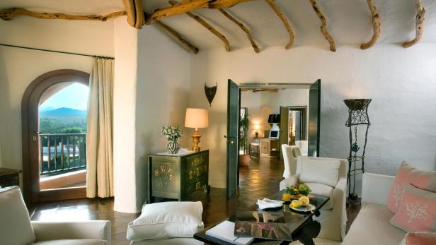 Ein Wohnzimmer mit weißen Möbeln, Holzbalken an der Decke und Blick auf eine grüne Landschaft.