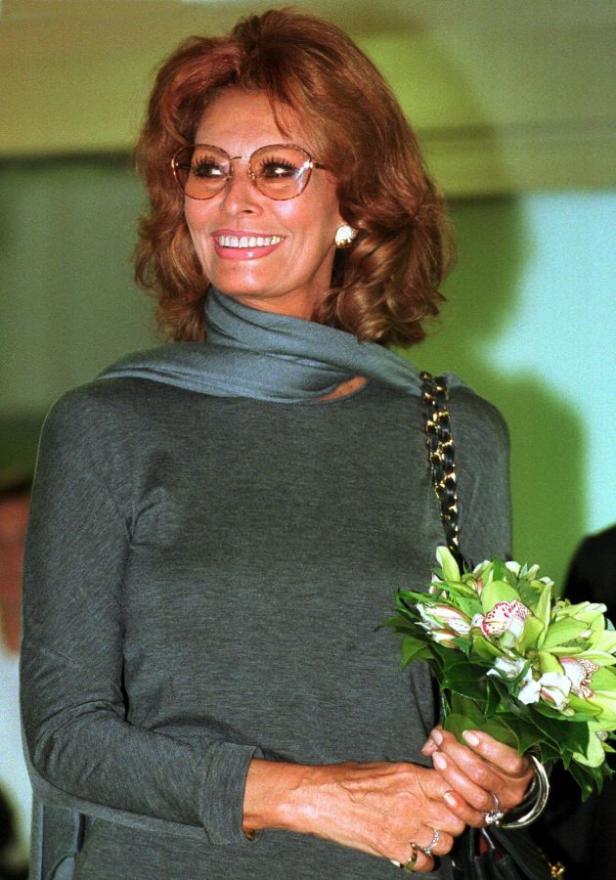 Sophia Loren lächelt und hält einen Blumenstrauß.