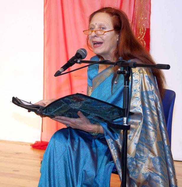 Eine Frau in einem blauen Sari liest von einem Mikrofon aus einem Buch vor.