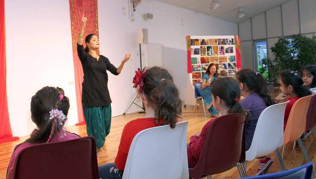 Eine Frau führt einen indischen Tanz vor einem Publikum aus Kindern auf.