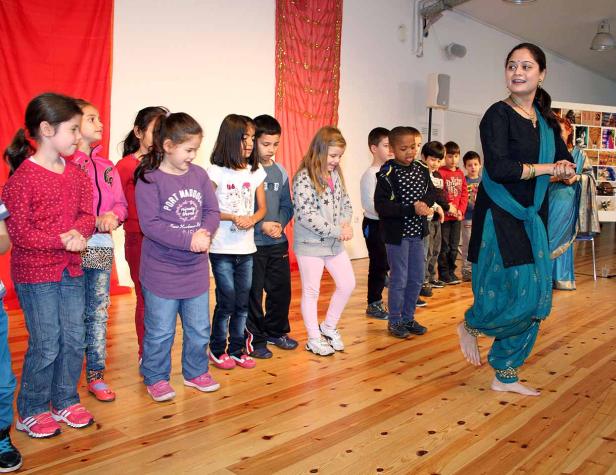 Eine Frau in traditioneller Kleidung tanzt vor einer Gruppe von Kindern.