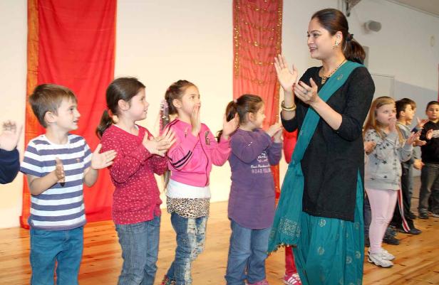 Eine Frau in traditioneller Kleidung klatscht mit einer Gruppe von Kindern.