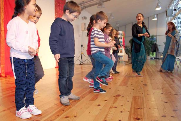 Eine Gruppe Kinder tanzt mit zwei Frauen auf einer Bühne.