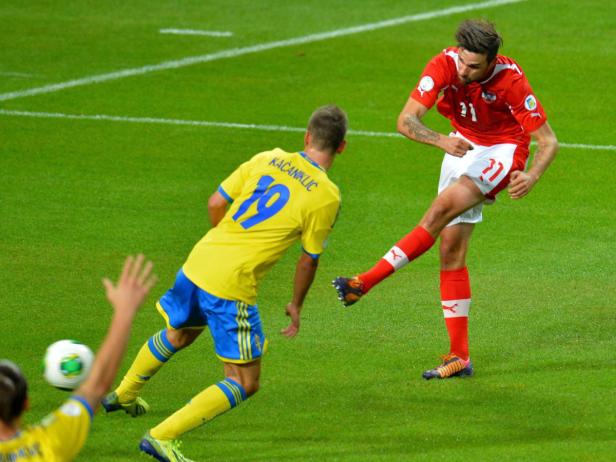 Ein österreichischer Fußballspieler schießt den Ball, während ein schwedischer Spieler zusieht.