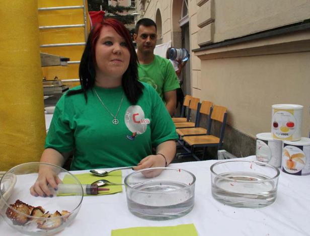 Eine Frau mit einem grünen T-Shirt steht an einem Tisch mit Schüsseln und Spritzen.