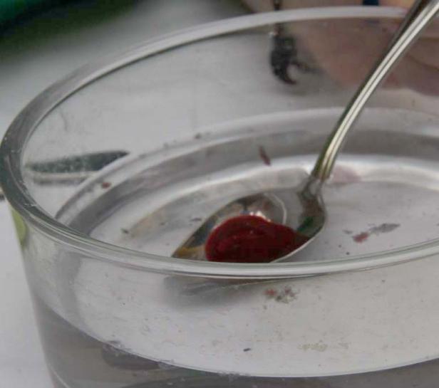 Ein Löffel mit roter Flüssigkeit in einem Glas Wasser.