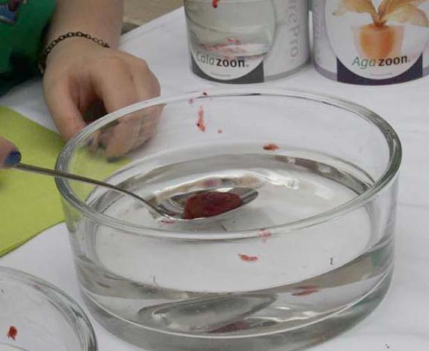 Eine Person hält einen Löffel mit einer roten Frucht über eine Schüssel mit Wasser.