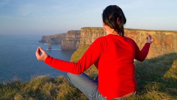 Eine Frau meditiert auf einer Klippe mit Blick auf das Meer.