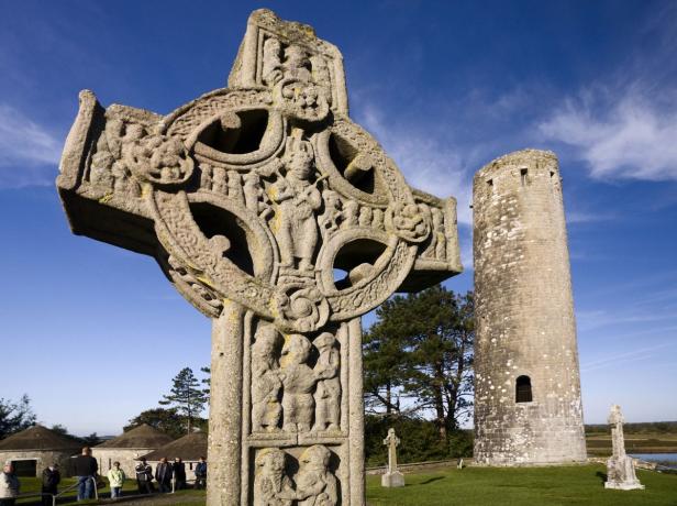 Ein verziertes Hochkreuz und ein Rundturm in einer irischen Landschaft.