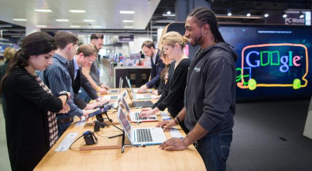 Eine Gruppe von Menschen testet Laptops an einem Stand mit einem Google-Logo im Hintergrund.