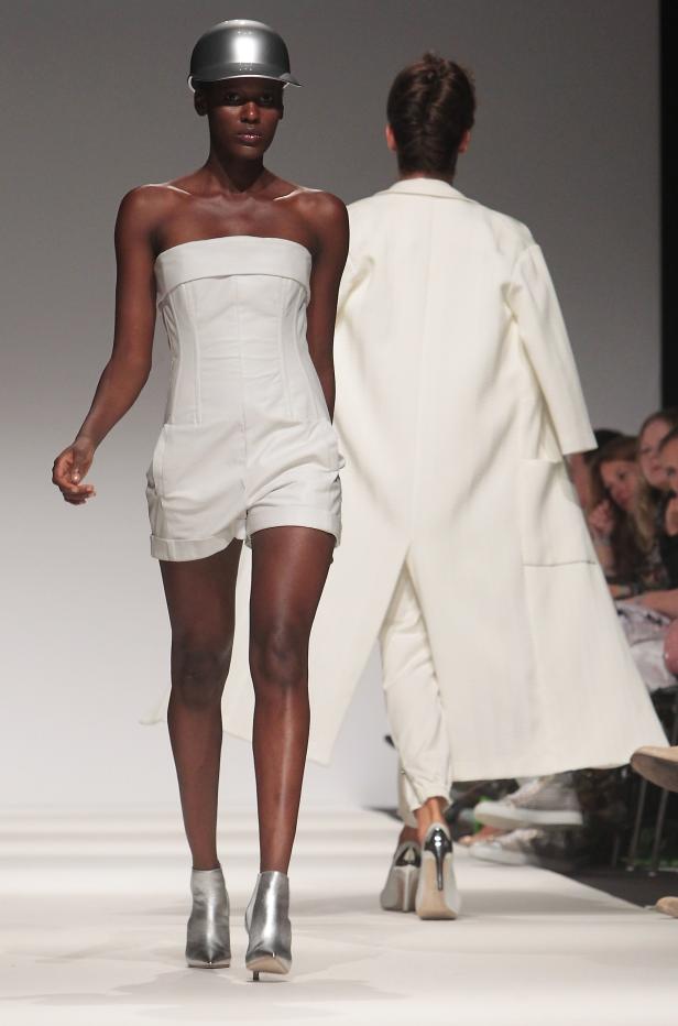 Eine dunkelhäutige Frau mit einem silbernen Helm und einem weißen Hosenanzug auf dem Laufsteg.