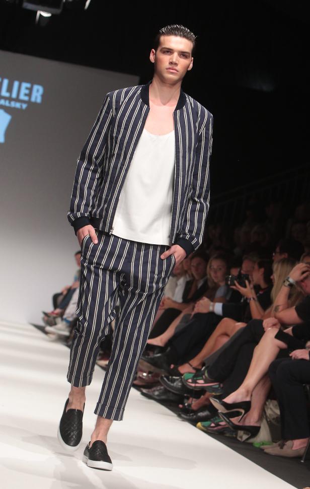Ein Mann präsentiert ein blau-weiß gestreiftes Outfit auf einem Laufsteg.