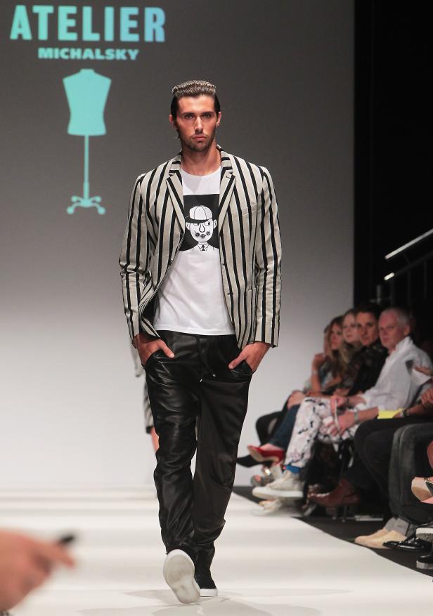 Ein Mann in einem gestreiften Sakko und Lederhose läuft über einen Laufsteg von Atelier Michalsky.