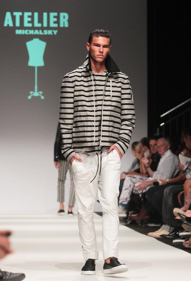 Ein Mann in gestreifter Jacke und weißen Hosen läuft auf einem Laufsteg.