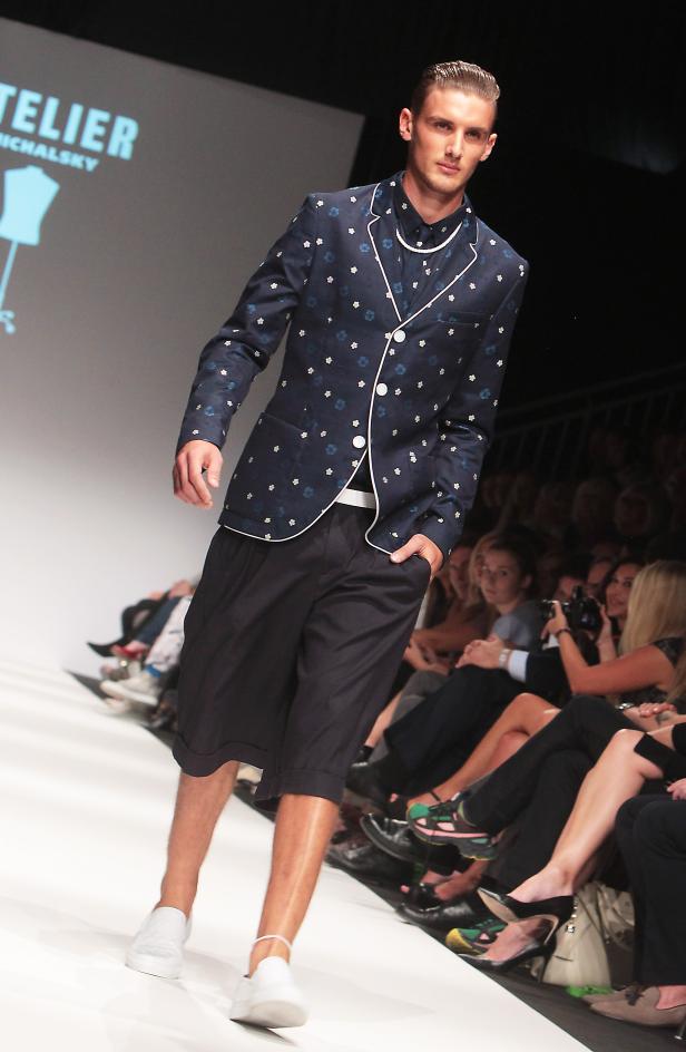 Ein Mann präsentiert ein blaues Sakko mit Blumenmuster und kurze, dunkle Hosen auf dem Laufsteg.